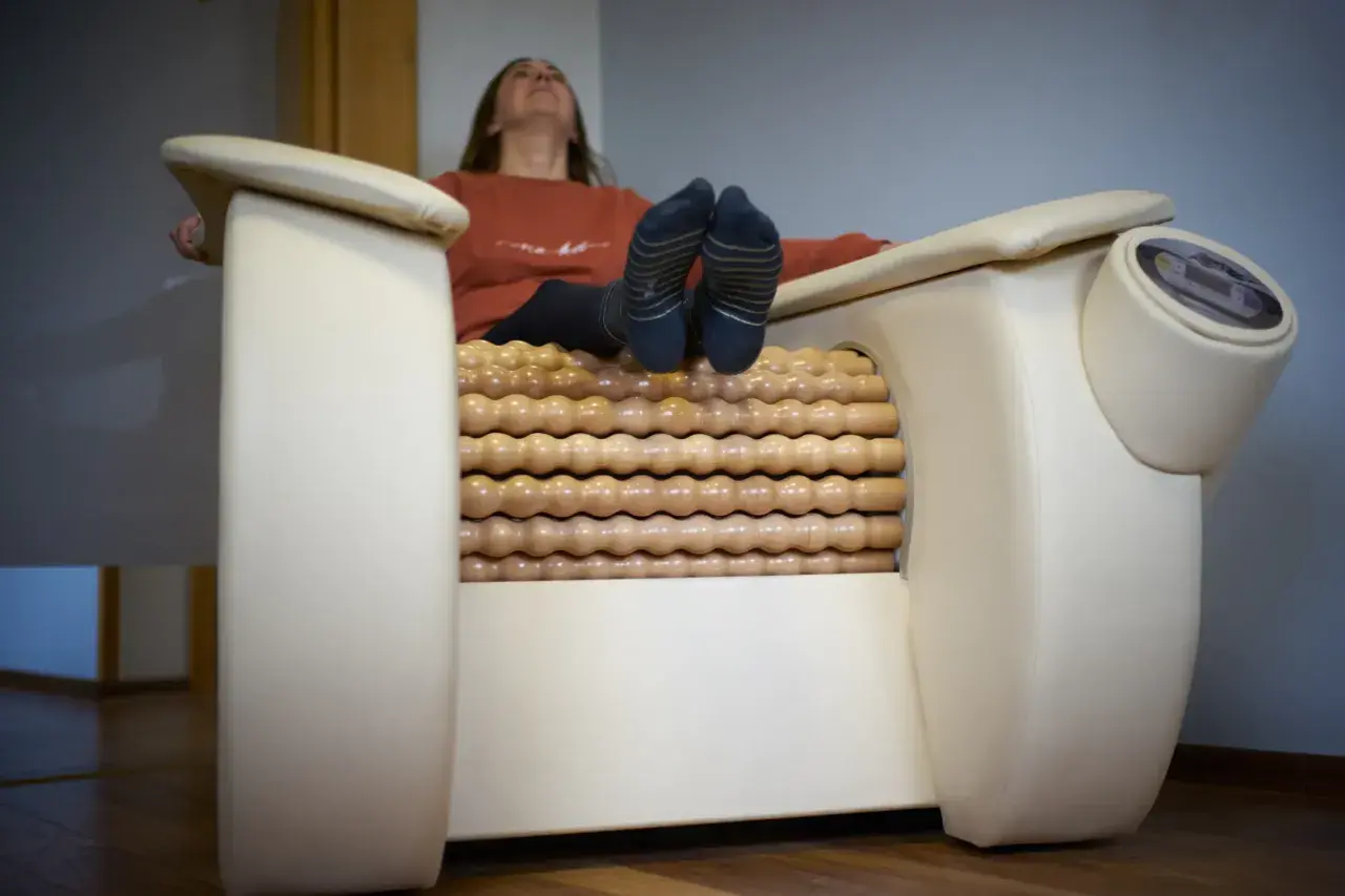 Kobieta relaksuje się na fotelu z masażem rolletic. Drewniane rolki masują jej nogi, podczas gdy ona unosi głowę do góry.