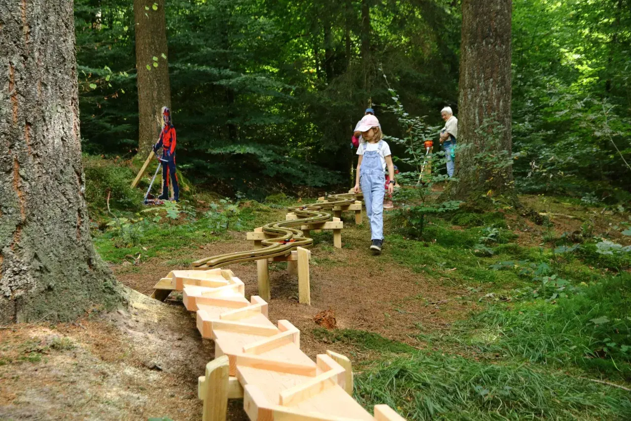 Ein Mädchen erkundet den erlebnispfad eifel kinder. Holzrinnen und eine Spielzeugbahn schlängeln sich durch den Wald.