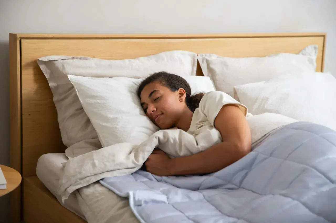 Joven durmiendo plácidamente, quizás gracias a la melatonina, envuelta en mantas y almohadas blancas.