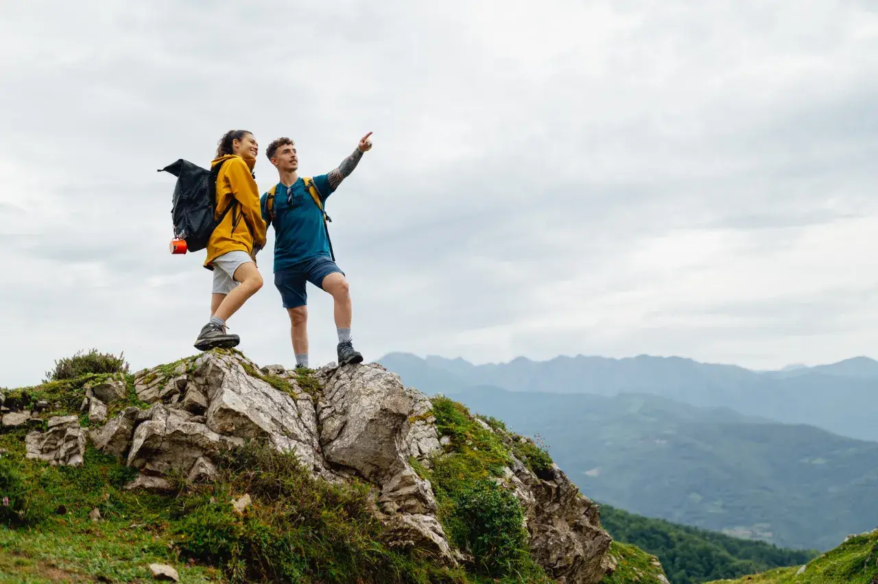 Zwei Wanderer auf einem Felsvorsprung genießen die Aussicht während ihrer Alpen Tour.