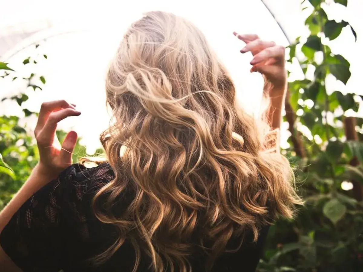 Cabello rubio con reflejos naturales, como si fuera babylights vs balayage. Manos en el aire, rodeada de vegetación.