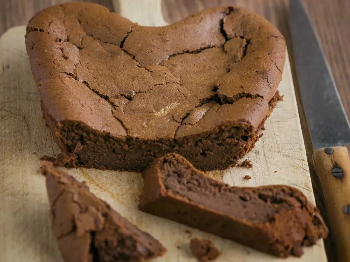 Un délicieux gâteau au chocolat en forme de cœur, un gâteau sans oeuf, craquelé sur le dessus, avec une part coupée.