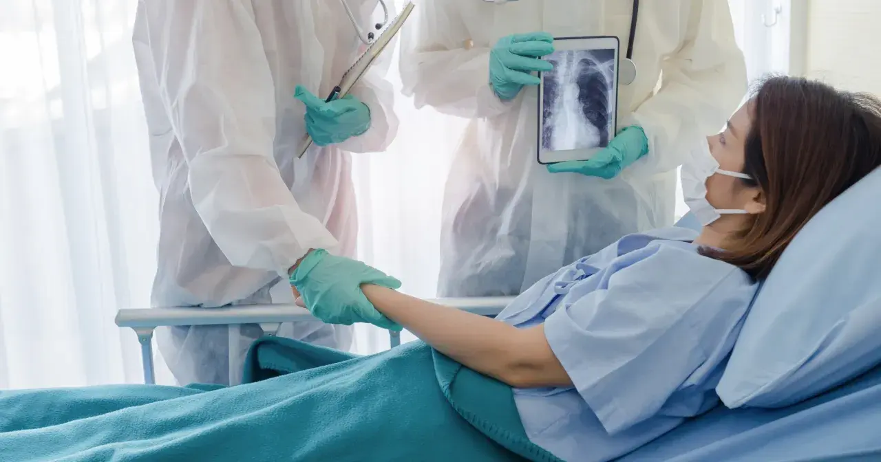Lekarze w kombinezonach ochronnych wspierają pacjentkę w szpitalu, pokazując jej zdjęcie płuc na tablecie. Nadzieja na powrót do zdrowia dzięki leczeniu, być może z użyciem remdesivir.