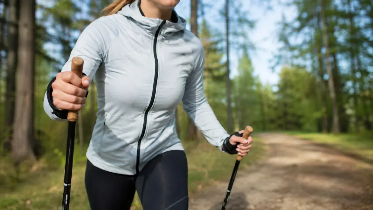 Kobieta z kijkami nordic walking w lesie. Dowiedz się, jak dobrać odpowiednie kijki do swojego wzrostu i stylu marszu.