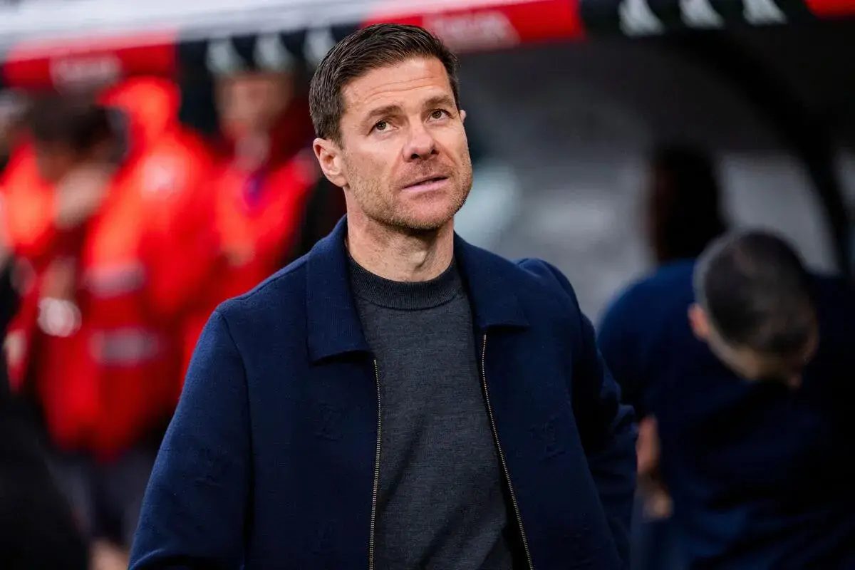Xabi Alonso, potencjalny trener Chelsea, w granatowej kurtce i szarym swetrze, z uwagą obserwuje boisko.