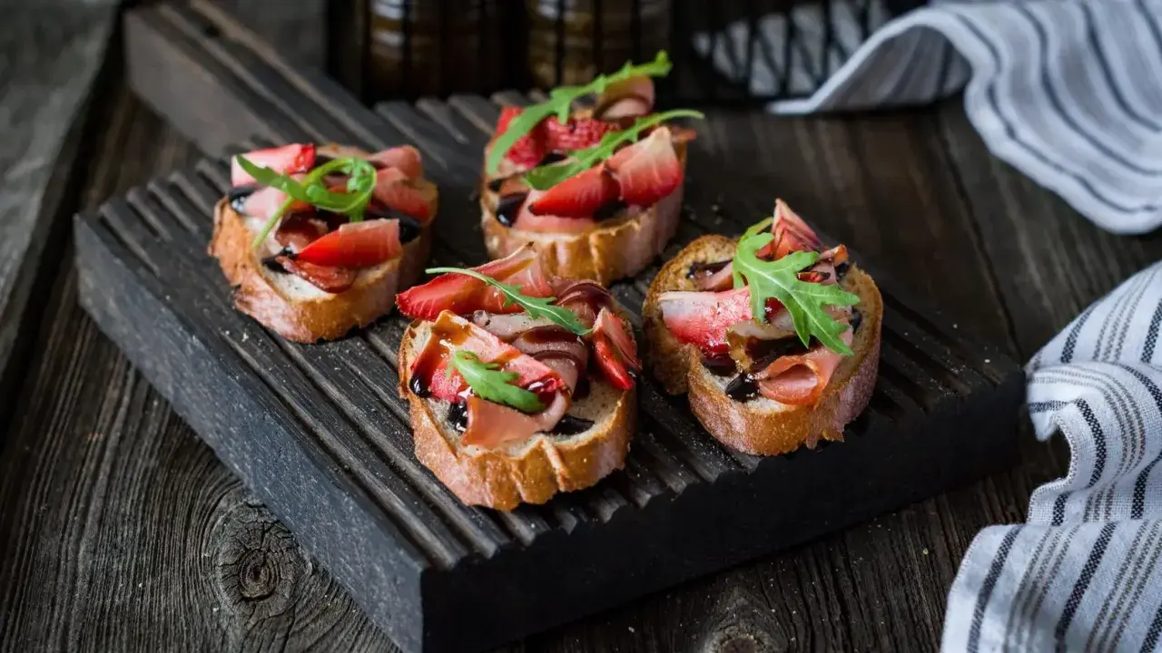 Bruschetta z truskawkami i szynką prosciutto, polana balsamicznym sosem. Idealny przepis na letnią przekąskę.