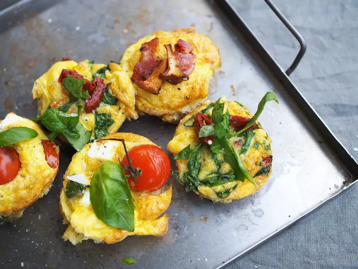 Matiga muffins med ägg, spenat, tomat och bacon på en plåt. Perfekt för en mättande frukost eller brunch.