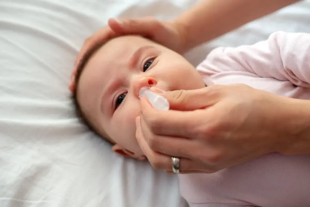 Mani che aiutano un neonato di 2 mesi con la tosse, somministrando gocce nasali per alleviare il naso chiuso.