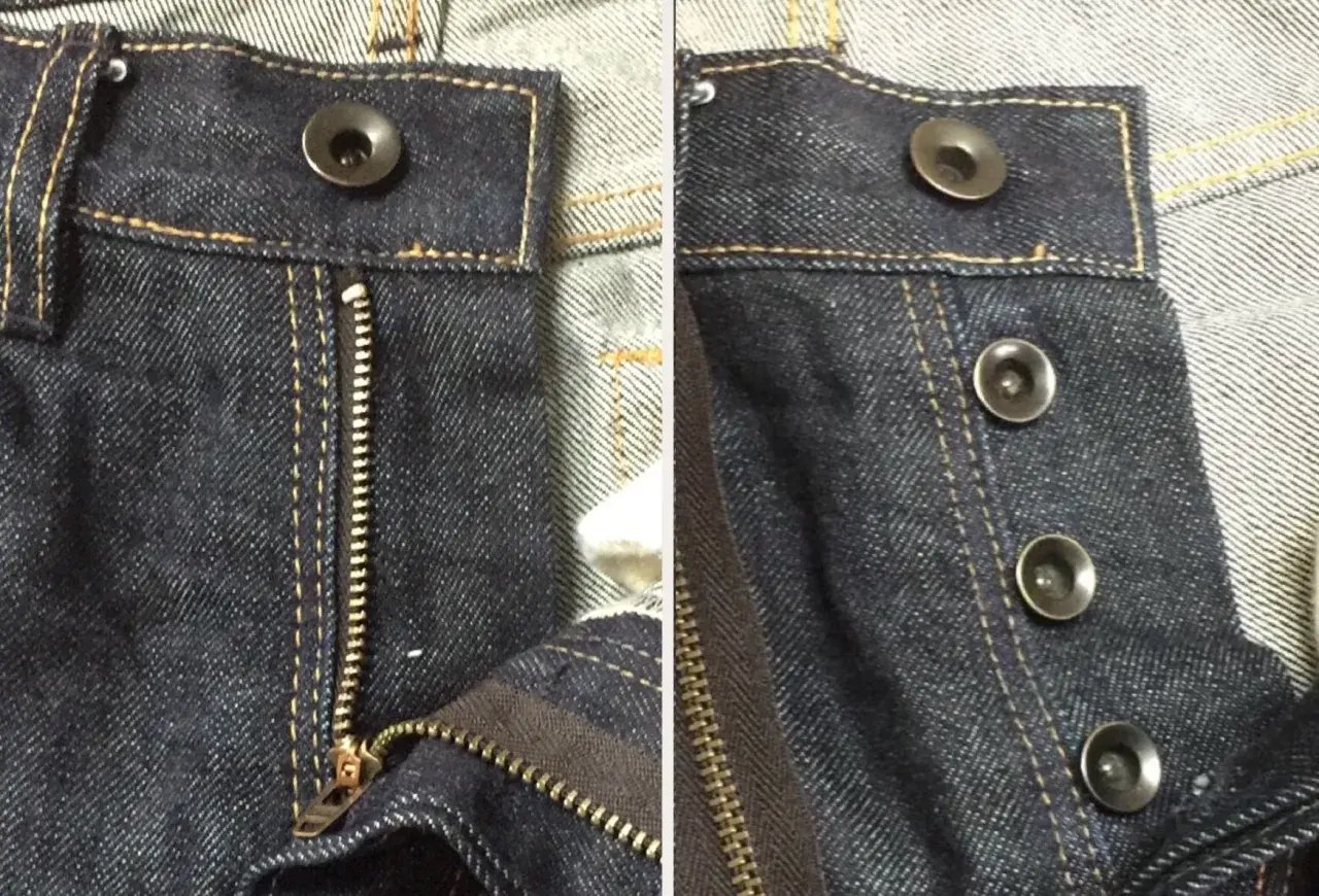 Close-up of dark wash jeans. One side shows a zipper fly with a single bouton jeans at the top. The other side displays three bouton jeans.