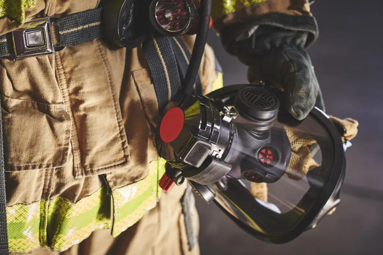 Bombero con equipo de protección, incluyendo una máscara y un compresor de aire respirable.