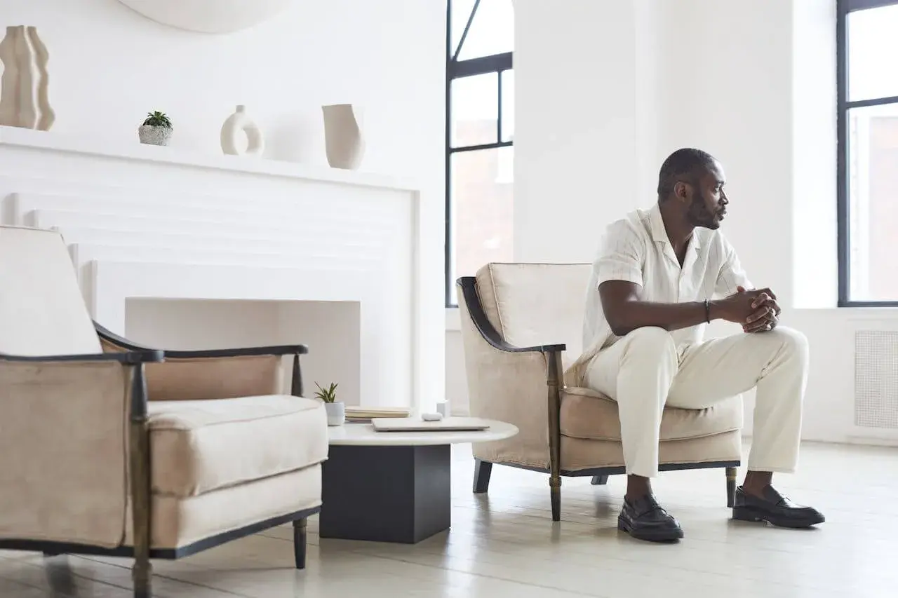Un homme élégant en tenue claire, assis dans un fauteuil, montre comment porter des mocassins avec style.