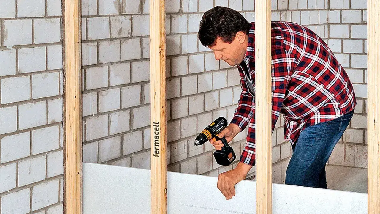 Mann baut eine Trockenbauwand mit Akkuschrauber und Gipskartonplatten.
