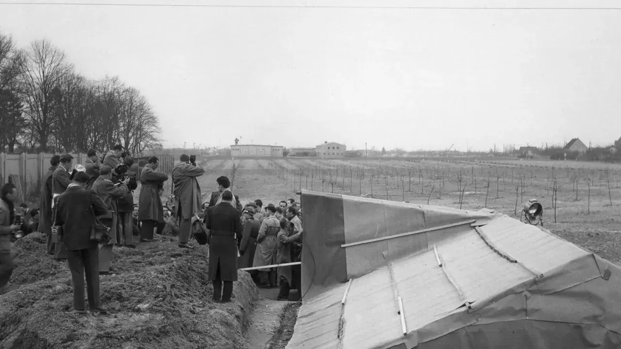 Eine Gruppe von Männern, darunter viele mit Kameras, versammelt sich um eine ausgegrabene Struktur. Ein Fall von Spionage im Kalten Krieg?