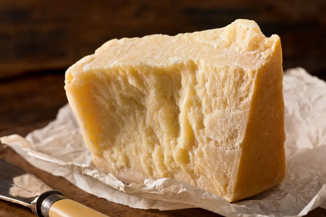 Un pezzo di formaggio stagionato, ideale per chi cerca un formaggio senza lattosio, su carta da forno con un coltello.