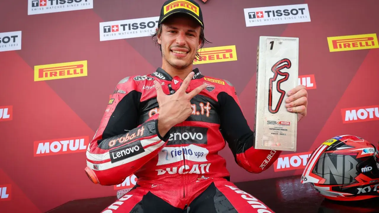 Nicolò Bulega, piloto de Ducati, celebra su victoria en Motorland Aragón con el trofeo y haciendo la señal de la victoria.