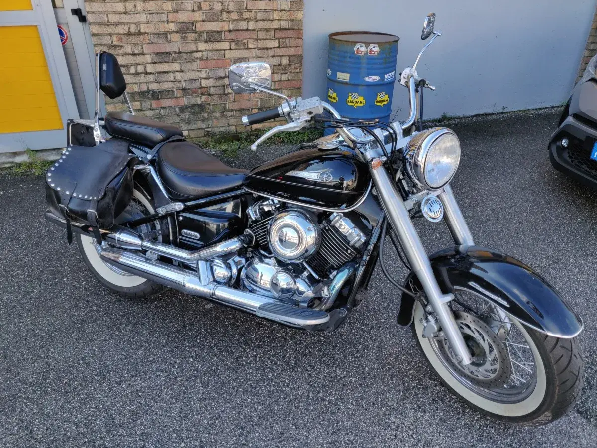Yamaha Dragstar 650 Custom nera, con borse in pelle borchiate e pneumatici a banda bianca, pronta per un viaggio.