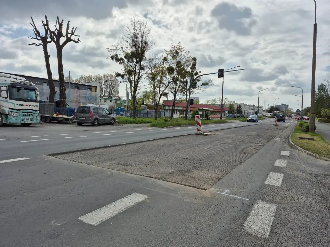Droga w Opolu z widocznymi pracami drogowymi, samochodami i drzewami.