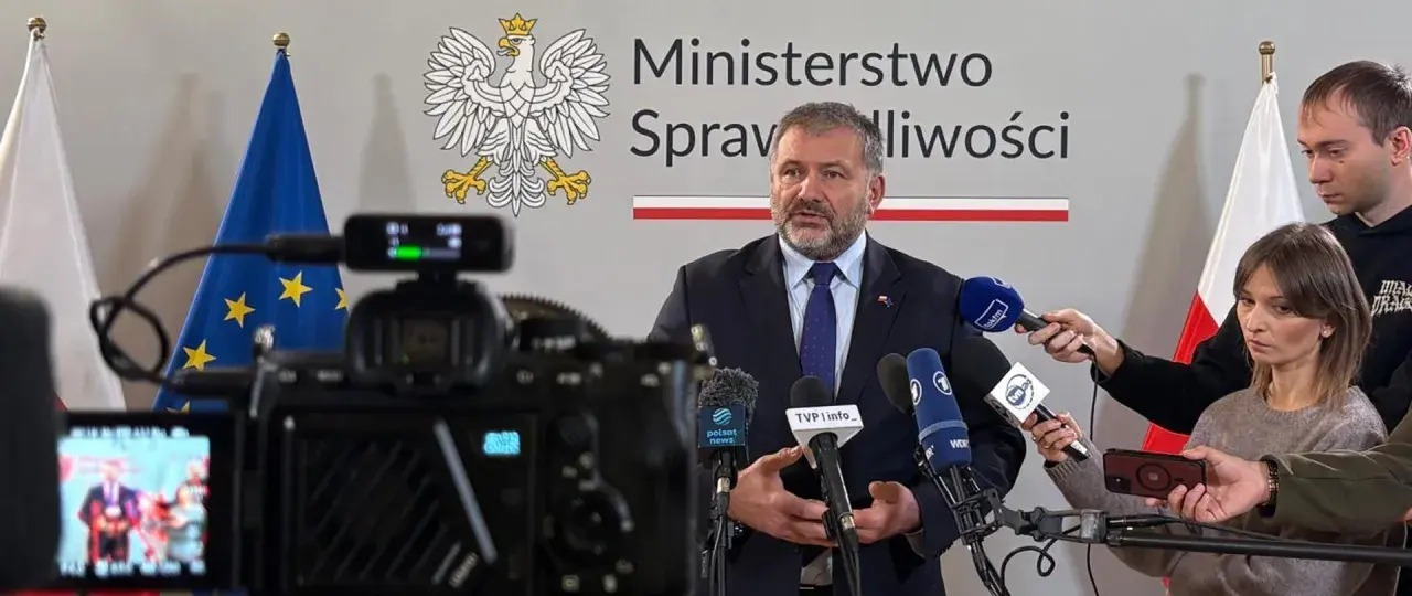 Minister sprawiedliwości przemawia do mediów, otoczony flagami Polski i UE. Dziennikarze zbierają materiał do reportażu o wyroku TSUE.