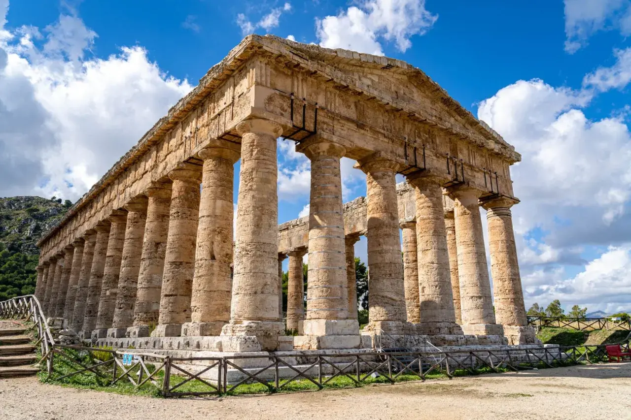 Ancient Greek temple ruins, a highlight of a 2 week Sicily itinerary, stand majestically under a blue, cloudy sky.