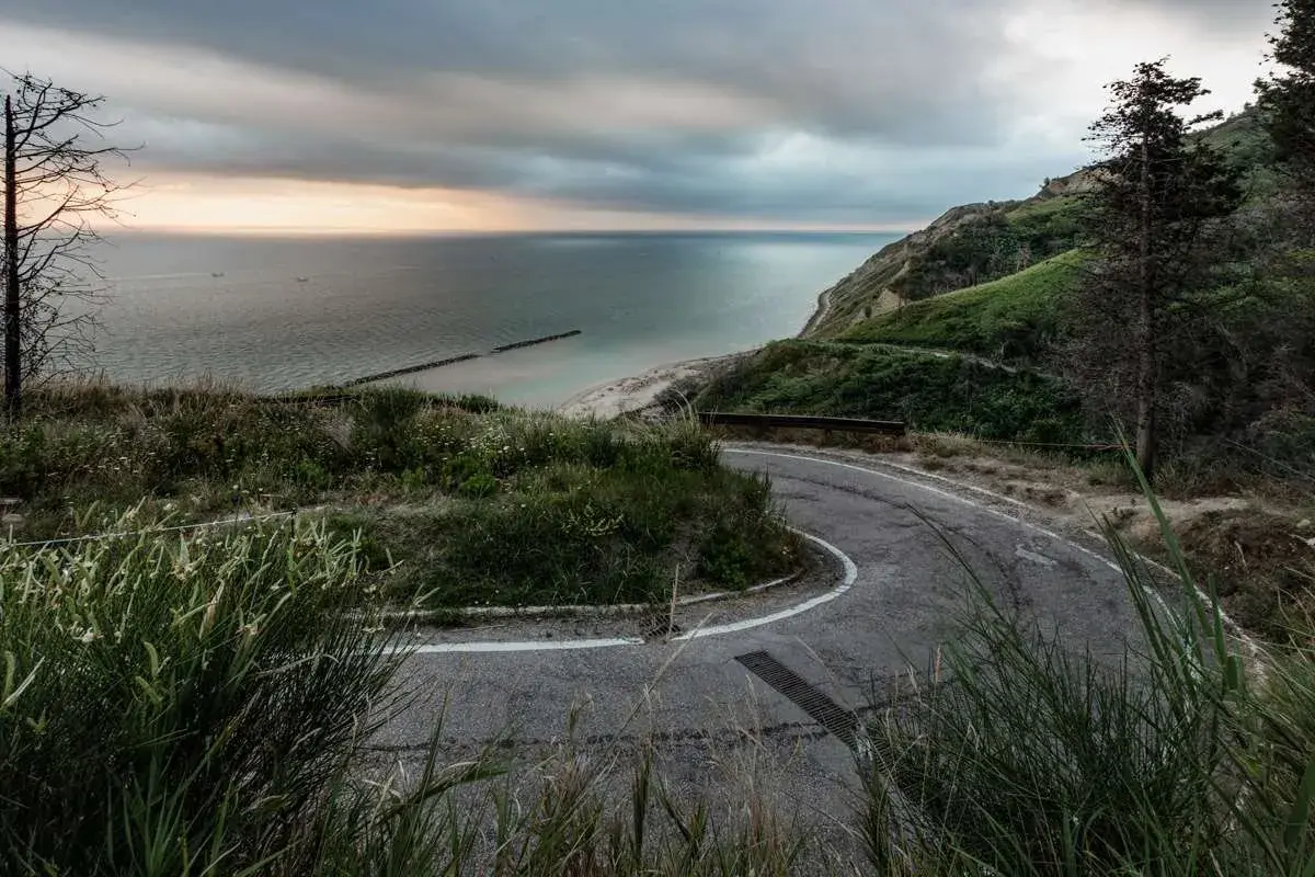 Strada tortuosa nel parco naturale regionale del Monte San Bartolo, con vista sul mare Adriatico e una spiaggia sabbiosa.