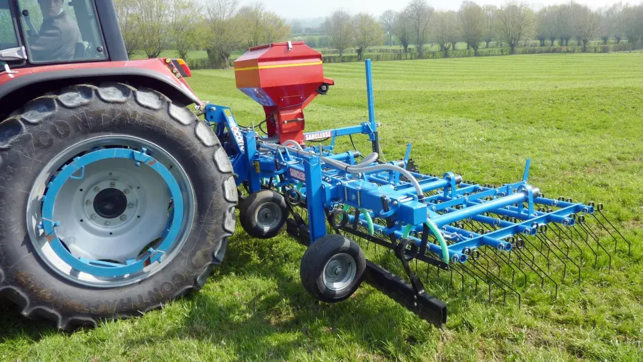 Tracteur rouge avec semoir bleu pour le sursemis de prairie. L'outil prépare le sol avant de semer de nouvelles herbes.