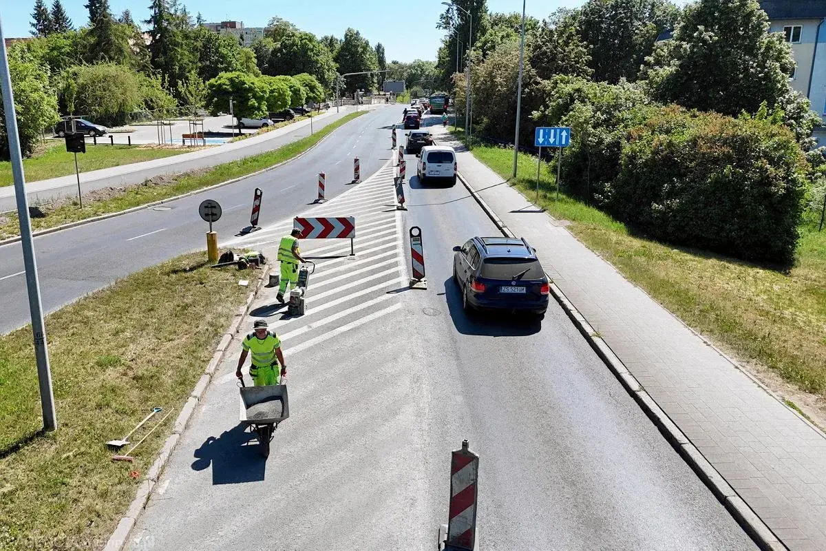 Prace drogowe na linii 101 w Szczecinie. Robotnicy w kamizelkach odblaskowych układają nawierzchnię, jeden z nich pcha taczkę z materiałem.