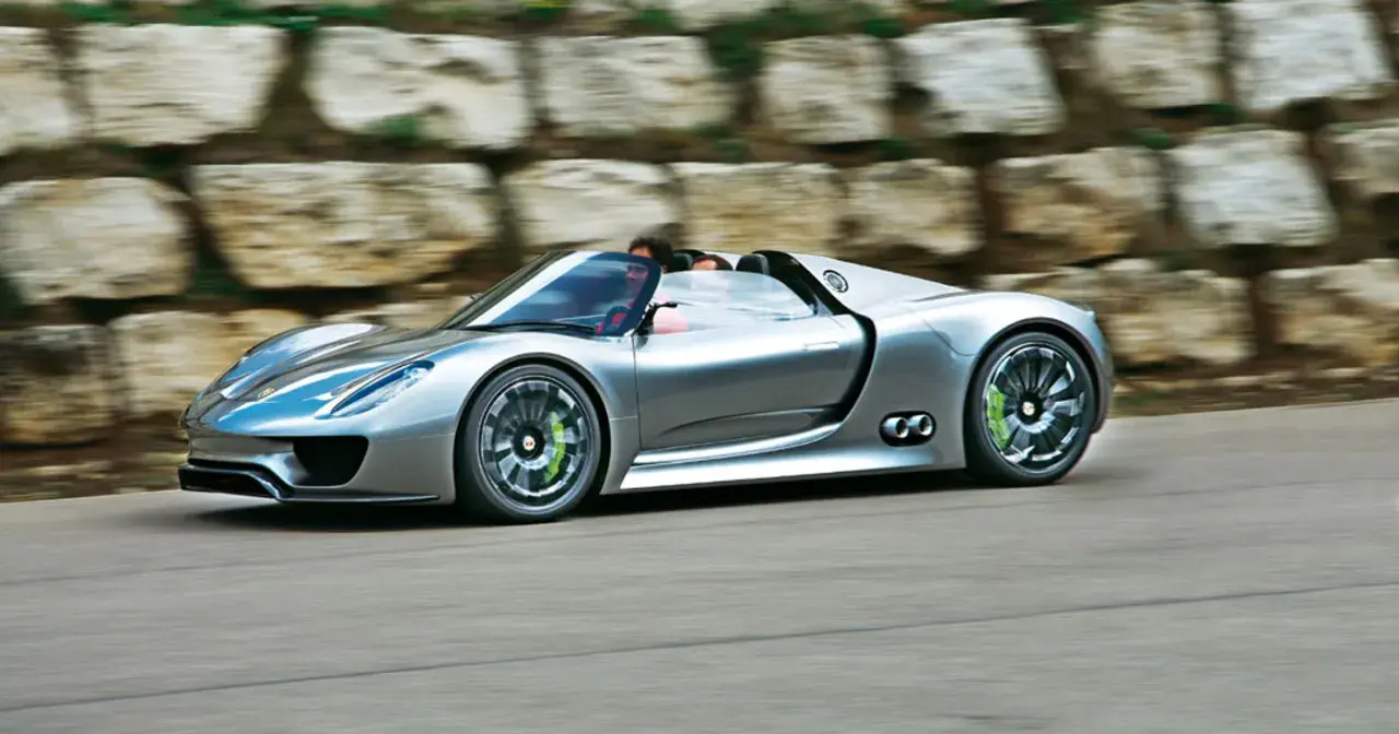 Srebrny Porsche 918 Spyder pędzi po drodze, z kierowcą za kierownicą.