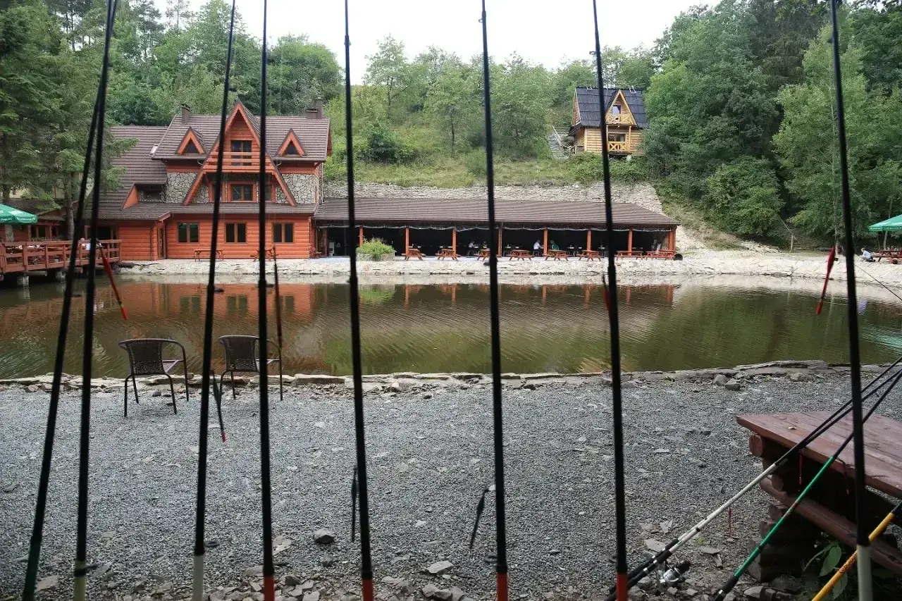 Wędki nad jeziorem z drewnianymi domkami i zadaszoną restauracją w tle.