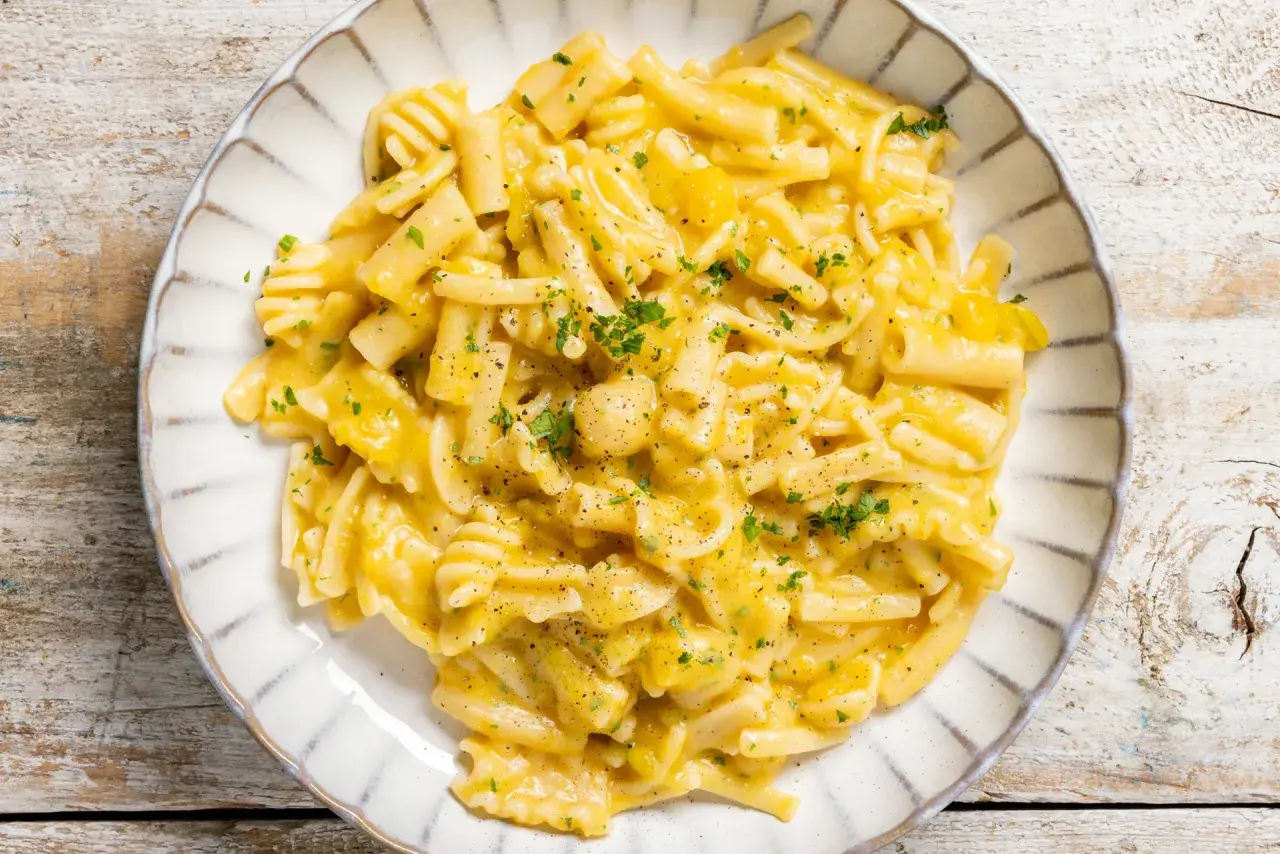 Piatto di pasta e zucca cremosa, guarnita con prezzemolo tritato e pepe nero, servita su un piatto bianco con bordo decorato.