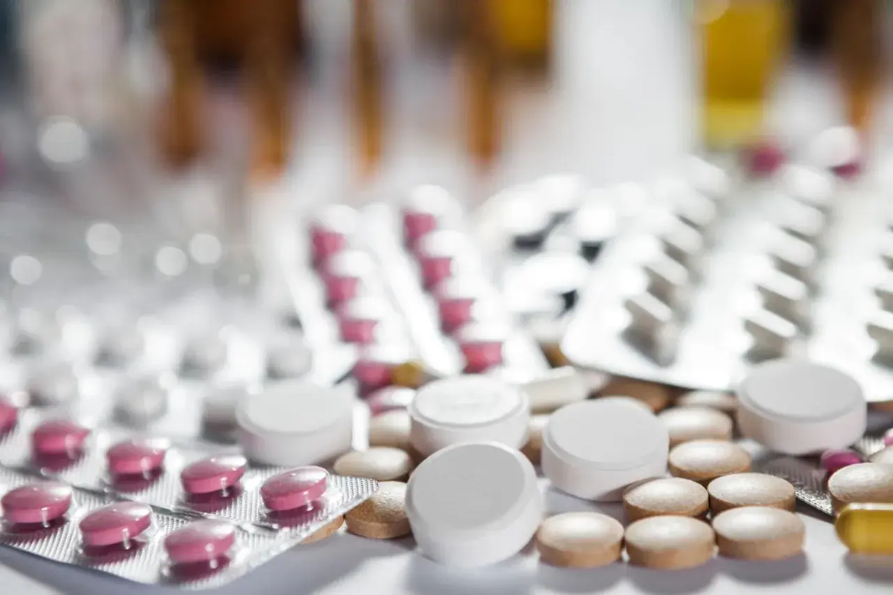 Zbliżenie na opakowania leków i tabletki, w tym różowe tabletki w blistrze i białe tabletki luzem. Może to być lek pramolan 50 mg.