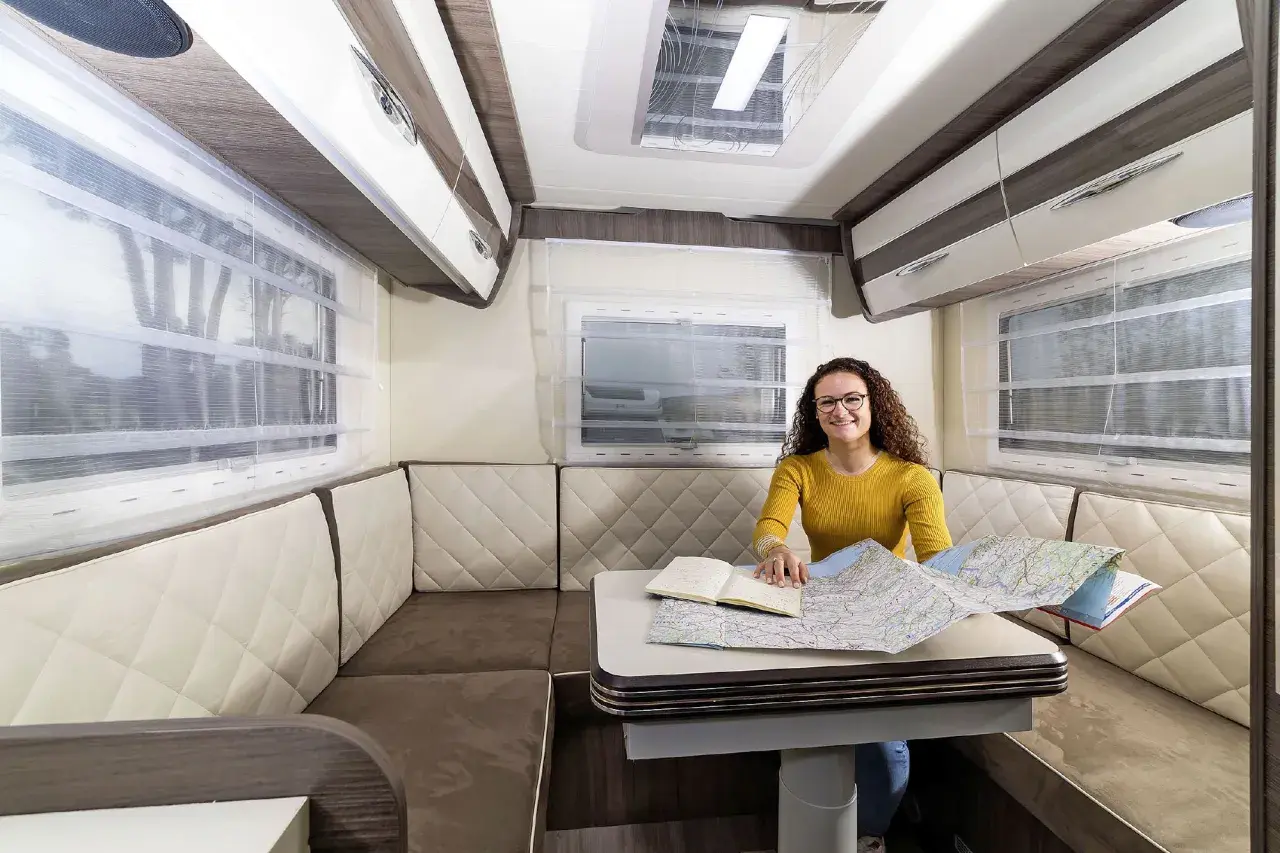 Aménagement du camping car salon arrière : une femme prépare son itinéraire sur une carte.