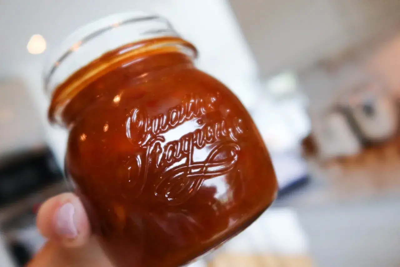 En hand håller ett glas med en mörkröd rabarber chutney. Texten "Quartier" och "Fragrance" syns i glaset.