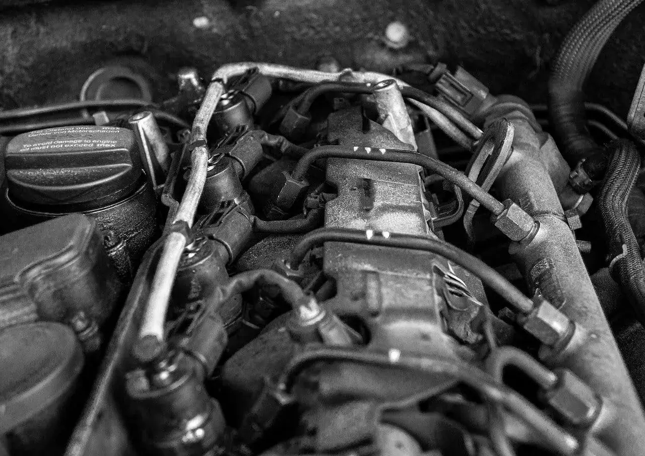 Silnik samochodowy, widok z góry. Widać przewody, wtryskiwacze i korek wlewu oleju z napisem "To avoid damage to engine oil must not exceed max". Może to oznaczać, że jest za dużo oleju w aucie.