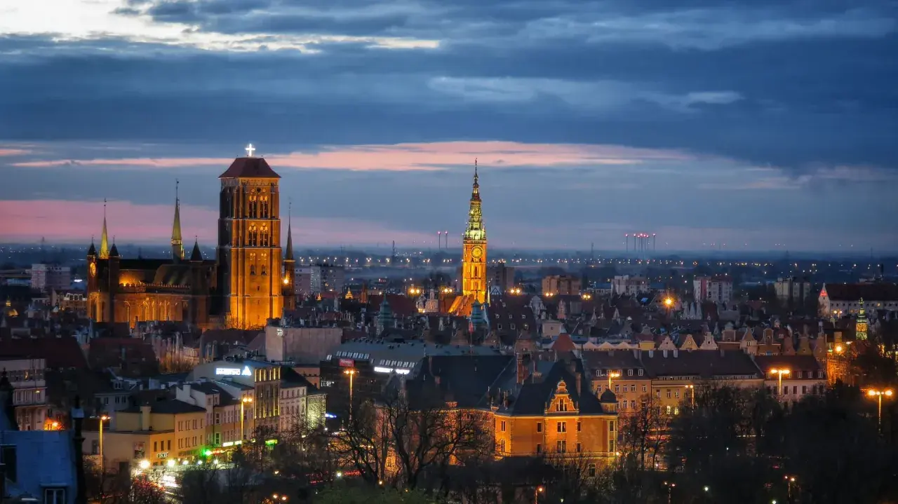 Wieczorny widok na zabytkowe centrum Gdańska, część m trójmiasto. Dominują iluminowane wieże Bazyliki Mariackiej i Ratusza Głównego Miasta.