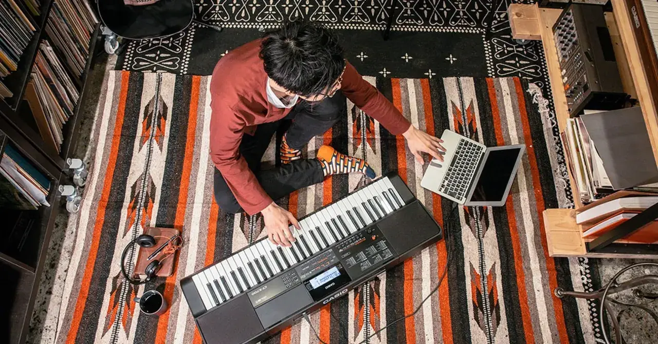 Mężczyzna gra na keyboardzie Casio, obok laptop i słuchawki.