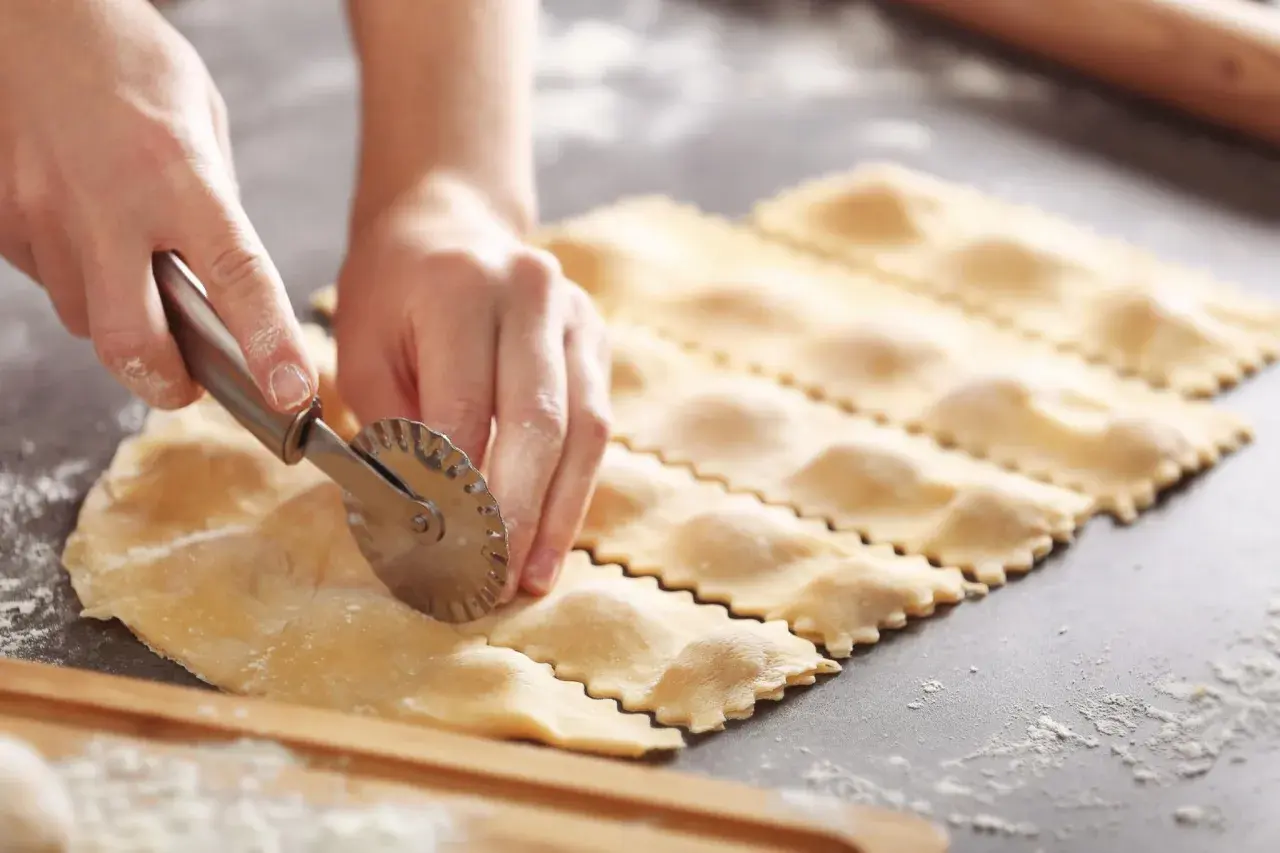 Hände schneiden mit einem Teigrädchen frische Ravioli. So einfach ist ravioli selber machen!