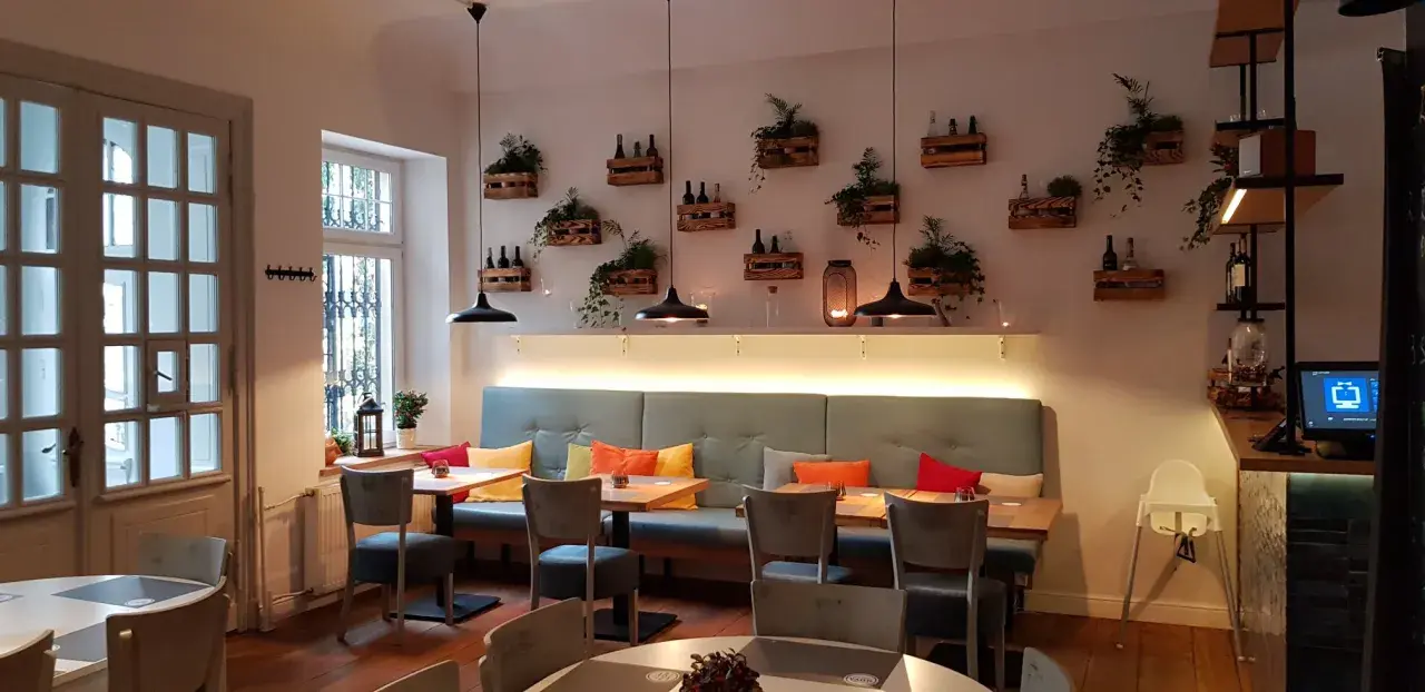 Przytulne wnętrze restauracji Nova Sopot z wygodnymi kanapami, drewnianymi skrzynkami z roślinami na ścianie i stylowymi lampami.