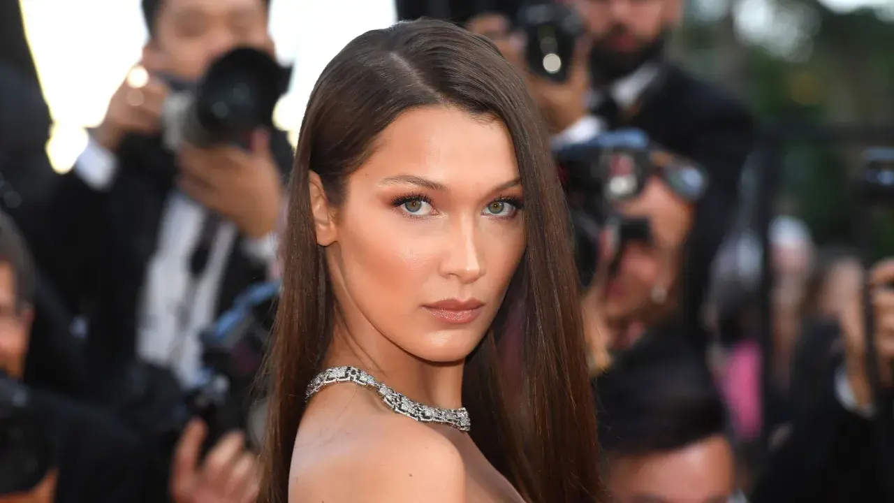Bella Hadid con un elegante side part, luciendo un collar de diamantes y rodeada de fotógrafos.