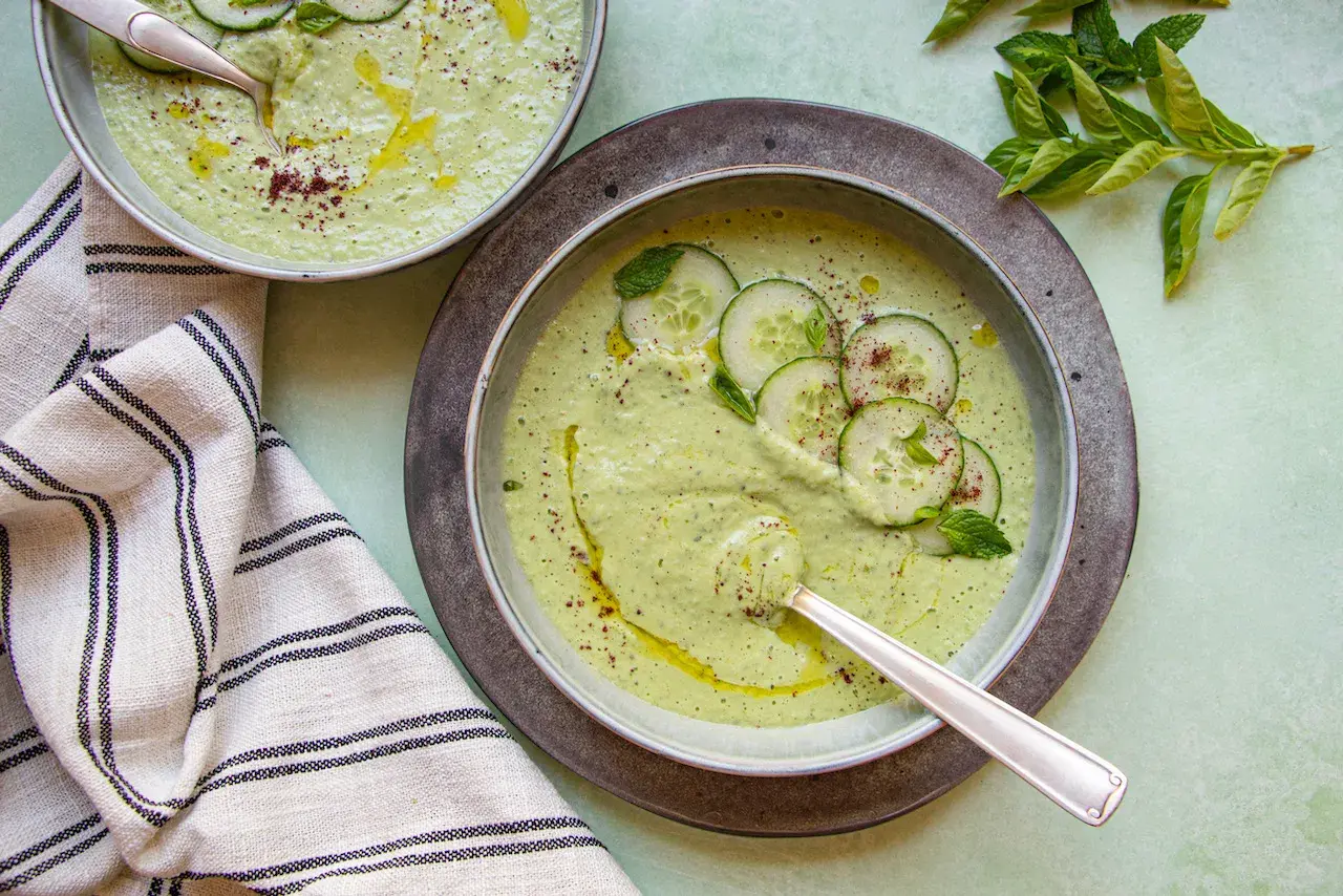 Deux bols de soupe froide aux concombres et menthe, arrosés d'huile d'olive et saupoudrés d'épices.