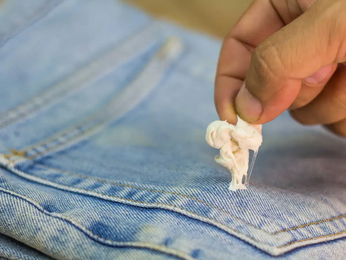 Maintenant, découvrez comment enlever du mastic sur un vêtement. Une main retire une boule de chewing-gum collante d'un jean bleu.