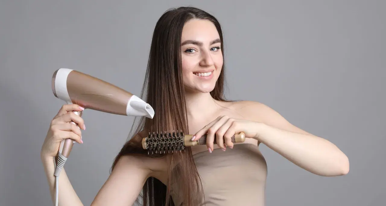 Kobieta suszy i modeluje włosy okrągłą szczotką i suszarką.