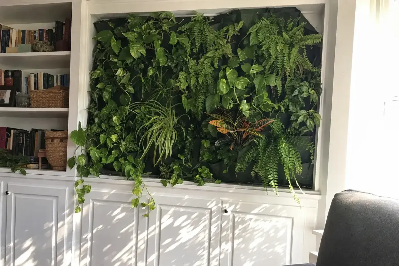 En frodig vägg med ormbunke inomhus och andra gröna växter, omgiven av bokhyllor och vita skåp.