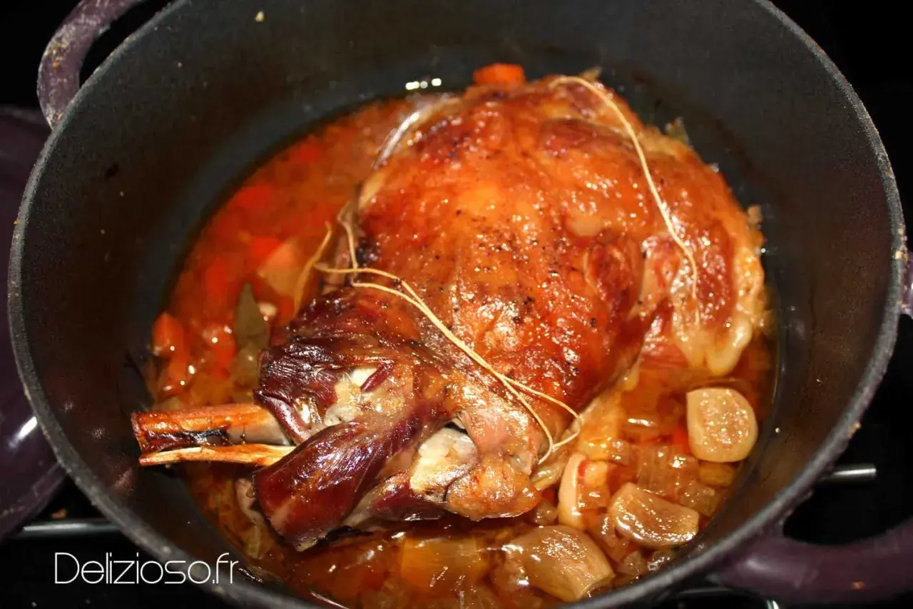 Une succulente épaule d'agneau rôtie dans sa cocotte, baignant dans un jus savoureux avec des oignons et des carottes.
