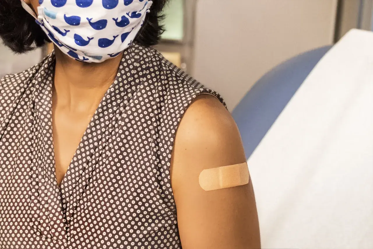 Osoba z maską na twarzy i plastrem na ramieniu po szczepieniu. Choć hpv szczepionka skutki uboczne są rzadkie, warto być świadomym.