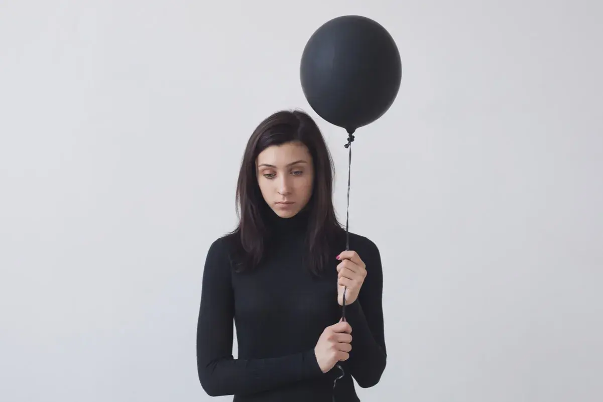 Donna con palloncino nero, espressione malinconica. Potrebbe rappresentare l'anedonia significato, la perdita di piacere.
