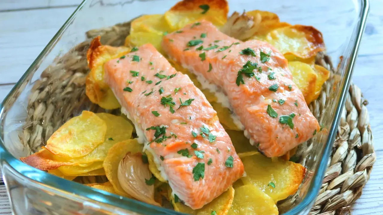Dos filetes de salmón al horno con patatas doradas y perejil picado, listos para servir.