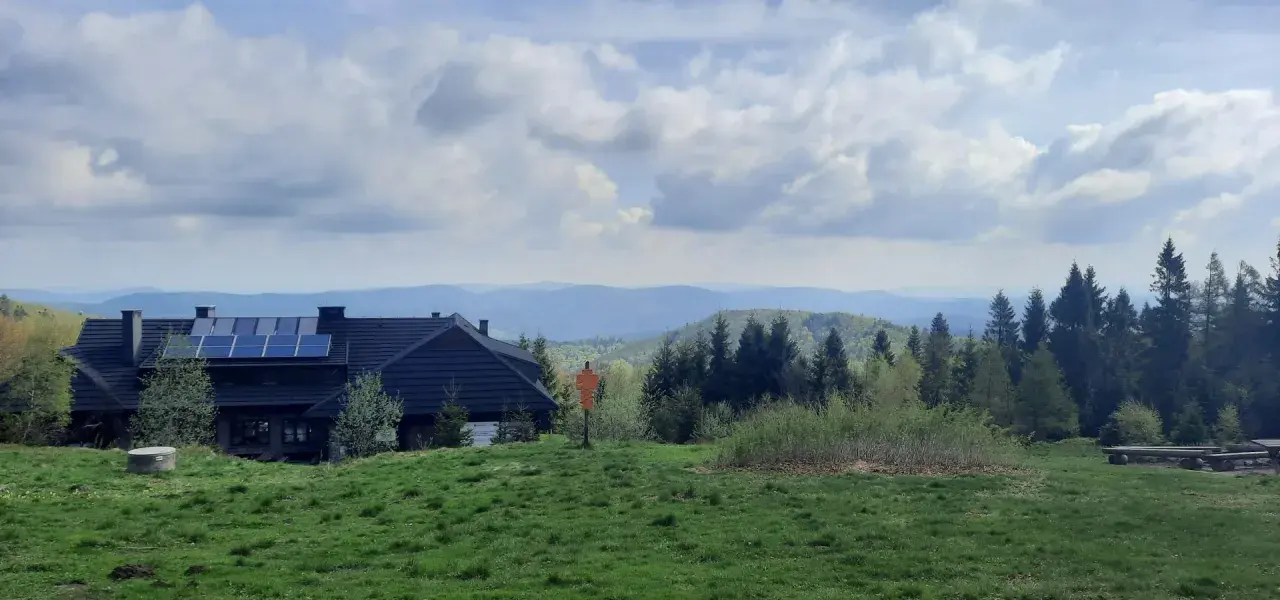 Dom z panelami słonecznymi na tle gór i lasów. Widok na szlaki Jaworzyny Krynickiej.
