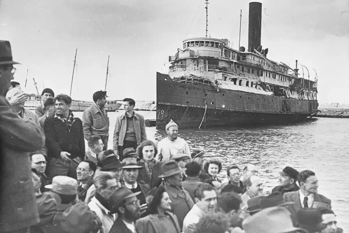 Folk samlas vid en skadad båt, en scen som speglar en del av israel historia.