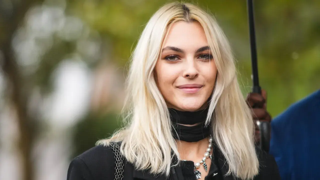Mujer joven con pelo rubio platino, ¿qué color de pelo me favorece? Suave sonrisa, collar de perlas y pañuelo negro.