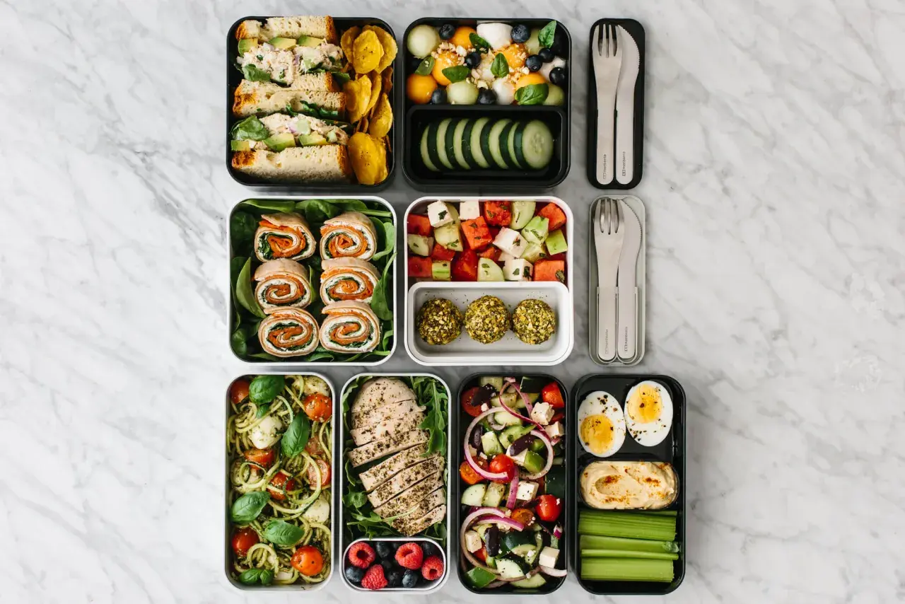 A colorful bento box diet spread with sandwiches, fruit salad, chicken, pasta, and snacks, perfect for a healthy lunch.